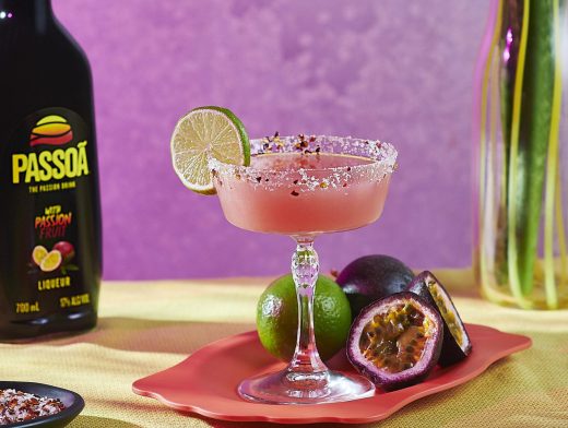 Passoã Spicy Margarita in coupe glass with lime garnish and Passoã bottle on pink background with passionfruits