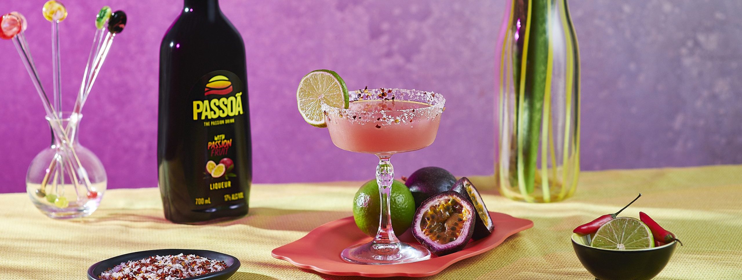 Passoã Spicy Margarita in coupe glass with lime garnish and Passoã bottle on pink background with passionfruits